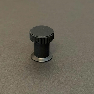 May include: A black cabinet knob with a round, ridged top and a cylindrical body. The knob has a small, flat base. The finish is matte black, and the knob appears to be made of metal.