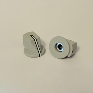 May include: Two grey control knobs with a white and black stripe detail. One knob is upright, showing the stripe, and the other is on its side, revealing a central metal insert. The knobs have a ridged texture on the sides.