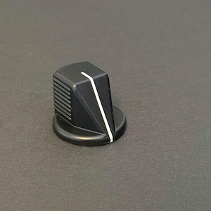 May include: A black control knob with a white line, likely for audio equipment. The knob has a ridged side and a circular base. The design is angular and modern, suitable for electronics or musical instruments.