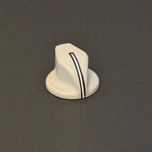 Op de afbeelding: Een lichtgrijze bedieningsknop met een zwart-witte streep. De knop heeft een ronde basis en een schuine bovenkant. Het ontwerp is eenvoudig en modern, geschikt voor diverse elektronische apparaten of huishoudelijke apparaten.