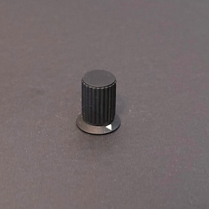 May include: A black control knob with a cylindrical body and a circular base. The body has vertical ridges, and the base features a white triangle indicating direction. This knob is likely for adjusting settings on electronic devices.