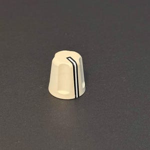 Pode incluir: Um botão de controle creme com um design de listras pretas e brancas. O botão tem formato cônico com a parte superior plana e provavelmente é usado para ajustar as configurações em equipamentos eletrônicos.
