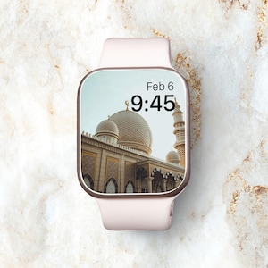 Op de afbeelding: Een roze smartwatch met een wit scherm dat de datum "Feb 6" en de tijd "9:45" weergeeft. De achtergrondafbeelding is een moskee met gouden koepels.