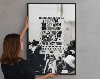 May include: Black and white framed poster with the text "I PRAY FOR THE DAY WHEN THE CHILDREN OF PALESTINE CAN WAKE UP TO THE SOUNDS OF BIRDS, NOT BOMBS." The poster is held by a person wearing a black shirt and jeans.
