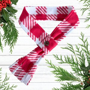 May include: A red and white plaid fleece scarf with a button closure. The scarf is made of soft material and has a classic pattern. The scarf is a winter accessory.