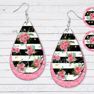 May include: A pair of pink and black teardrop-shaped earrings with a floral pattern and gold glitter accents. The earrings are made of resin and have a silver hook.