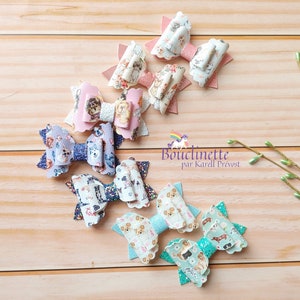 May include: A set of 8 colourful hair bows with a variety of dog patterns. The bows are made of fabric and have a scalloped edge. The bows are arranged in a semi-circle on a wooden surface.