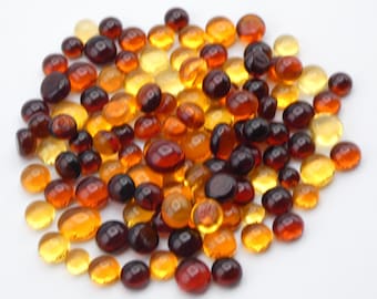 May include: A pile of amber glass stones in various shades of brown, orange, and yellow. The stones are oval shaped and have a smooth, polished finish.