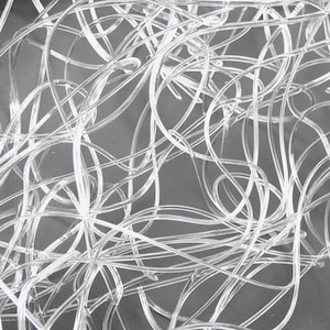 May include: A collection of thin, clear, flexible plastic tubing strands tangled together in a chaotic, overlapping arrangement. The transparent material reflects light, creating a series of curved lines and loops across the frame.