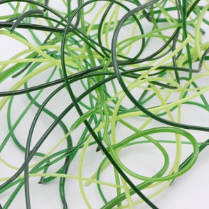 May include: A collection of thin, flexible, and smooth plastic strands in various shades of green, including dark forest green, lime green, and bright yellow-green, intertwined in a dense, chaotic, and overlapping arrangement.