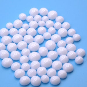 May include: A group of white, round, ceramic beads on a light blue background.