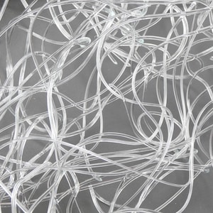 May include: A close-up shot of a tangled mass of clear, flexible tubing. The tubes are intertwined and create a complex, abstract pattern against a gray background. The transparent material allows light to pass through, highlighting the curves and loops.