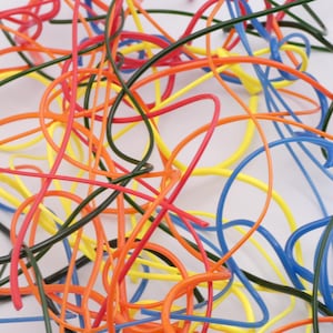 May include: A tangled collection of thin, flexible plastic wires in vibrant primary and secondary colors, including bright red, sunny yellow, deep blue, dark green, and neon orange, all intertwined in a chaotic, overlapping, and knotted arrangement.
