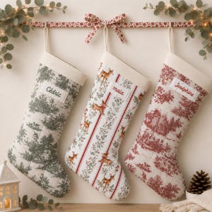 Pode incluir: Três meias de Natal penduradas numa barra. A meia da esquerda tem um padrão toile verde e o nome Cédric. A meia central apresenta um padrão de veados e riscas florais com o nome maia. A meia da direita tem um padrão toile vermelho e o nome Joséphine.