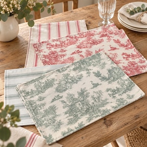 Op de afbeelding: Een collectie rechthoekige stoffen placemats met diverse patronen. De set bevat placemats met rood-witte strepen, rode toile de jouy-prints, groen-witte strepen en groene toile de jouy-prints op een lichte, crèmekleurige achtergrond.