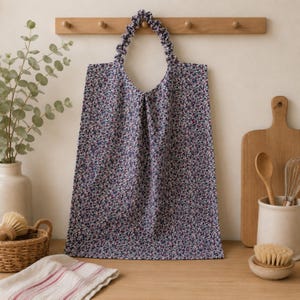 Peut inclure: Un essuie-main suspendu en tissu bleu foncé orné d'un motif floral dense et multicolore. L'essuie-main est doté d'une boucle en tissu froncé de type chouchou sur le dessus pour le suspendre, conçu pour tomber verticalement depuis un crochet.