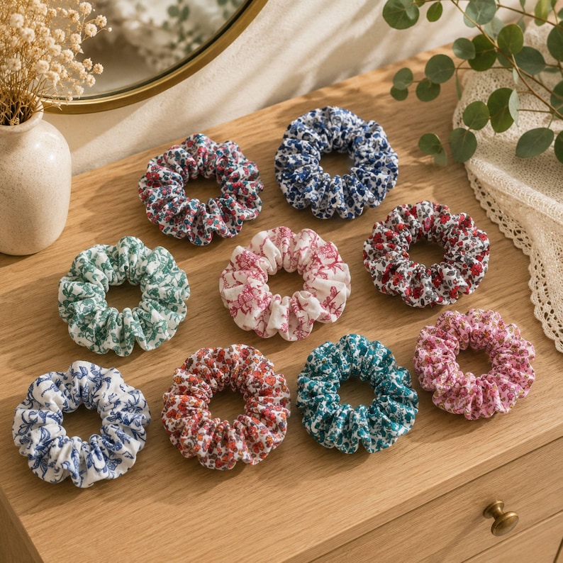 K&ouml;nnte beinhalten: Eine Sammlung von neun Haargummis aus Stoff mit verschiedenen Blumen- und Toile-Mustern in Farben wie Blau, Gr&uuml;n, Rot, Rosa und Wei&szlig;. Jedes Haargummi hat ein gerafftes, elastisches Design mit einem ger&uuml;schten Rand und individuellen Drucken.