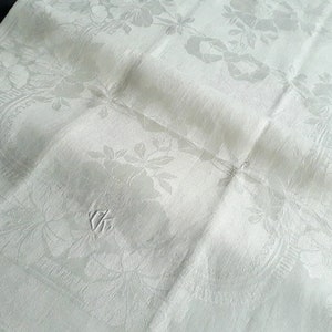 May include: A white linen napkin with an embroidered floral design. The napkin is folded in half and has a subtle sheen.