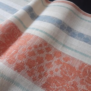 Pode incluir: Toalha de cozinha de linho branco com um padrão floral vermelho e branco e listras azuis e verdes.