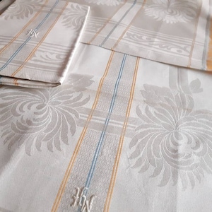 May include: Cream and white tablecloth and napkins with a floral design and yellow and blue striped details. The napkins and tablecloth have the embroidered initials "HW".