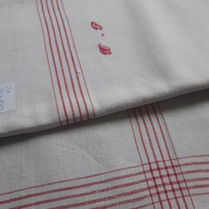 Op de afbeelding: Twee witte linnen theedoeken met rode strepen. De bovenste theedoek heeft een rood geborduurd monogram.
