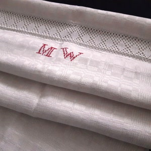 Pode incluir: Toalha de chá de linho branco com um monograma bordado a vermelho "MW". A toalha tem uma borda de renda e um padrão xadrez.