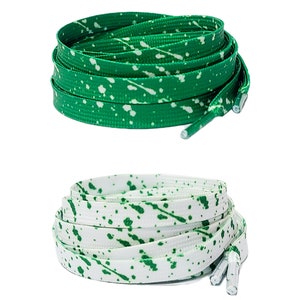 Può includere: Due paia di lacci con un motivo a spruzzo verde e bianco. La coppia superiore è verde con spruzzi bianchi, e la coppia inferiore è bianca con spruzzi verdi.