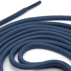 May include: Close-up of navy blue shoelaces. The laces are coiled, showing a woven texture. The aglet is black. The shoelaces are a solid color and appear to be made of a durable material.