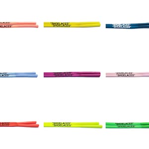 Puede incluir: Nueve pares de cordones de zapatos en varios colores, incluyendo rosa, azul, verde, amarillo y rojo. Cada par tiene el texto "SHOELACES" impreso en ellos.
