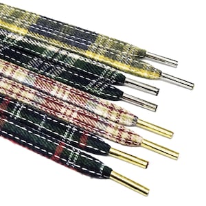Puede incluir: Primer plano de varios cordones a cuadros en varios colores, incluyendo verde, amarillo y rojo. Los cordones tienen punteras metálicas en los extremos y están dispuestos diagonalmente sobre un fondo blanco. El patrón a cuadros es un diseño clásico.