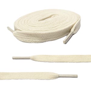 May include: A roll of cream-colored shoelaces with a flat, woven design. Two additional shoelaces are shown below, with the aglets visible. The shoelaces are a neutral color, suitable for various shoe styles.
