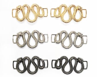 May include: Three pairs of snake-shaped metal shoe buckles. The buckles are in gold, silver, and black.