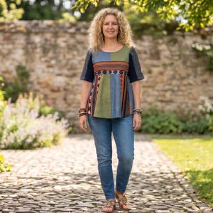 May include: A short-sleeved blouse featuring a color-blocked design in shades of blue, green, and dark gray, accented with a horizontal patterned band across the chest, paired with blue denim jeans and brown sandals.