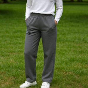 May include: A person wearing a white long-sleeve shirt and gray sweatpants with pockets. The sweatpants have a drawstring waist and are paired with white sneakers. The background is green grass.