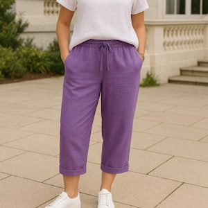 May include: A person wearing a white t-shirt and purple cropped pants with a drawstring waist and cuffed hems. The person is also wearing white sneakers.