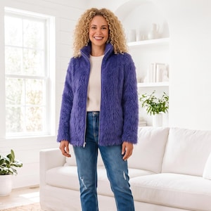 May include: A vibrant purple zip-up jacket with a long-pile faux fur texture, featuring a high collar and long sleeves. The jacket is worn over a plain white top and paired with blue denim jeans that have subtle distressed details on the legs.