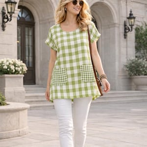 May include: A green and white checkered tunic with short sleeves and two front pockets. The tunic is paired with white pants. The woman is wearing sunglasses and carrying a brown purse.