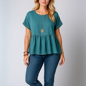 May include: Teal short-sleeved top with a round neck and peplum detail, paired with blue jeans. A long necklace with a circular pendant and bracelets are also visible. Measurements are in cm.
