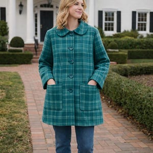 May include: A teal plaid coat with a rounded collar and large buttons. The coat has two front pockets and is worn with blue jeans. The coat is knee-length and the plaid pattern is a mix of teal and green.