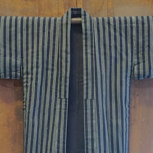 May include: A black and green striped kimono with a long sleeve design. The kimono is hanging on a wooden wall.