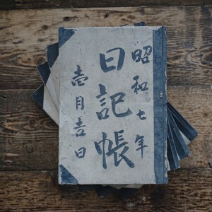 May include: A stack of old, worn books with a blue and white cover. The cover features Japanese characters in black ink. The characters read "白話 唱歌".