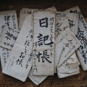 Peut inclure: Une pile de vieux documents en papier blanc avec de la calligraphie à l'encre noire. Les documents sont écrits en japonais. Les documents sont sur une surface en bois.
