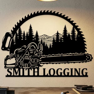 Peut inclure: Décoration murale en métal noir représentant une tronçonneuse, une silhouette de montagne et de forêt, et le texte "SMITH LOGGING". Le design est placé sur un fond clair, avec une forme de lame de scie circulaire en haut. Un établi et des outils sont au premier plan.