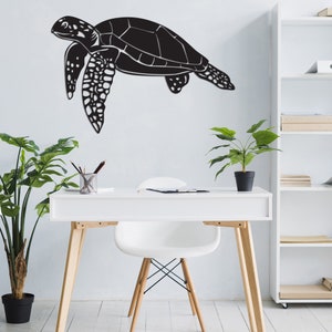 May include: A black metal sea turtle wall art piece. The turtle is depicted in a side profile, with detailed flippers and shell segments. The art is mounted on a white wall, above a white desk with plants.