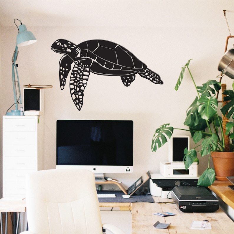 May include: A large black sea turtle wall decal. The turtle is depicted in a side profile, with detailed flippers and shell. The decal is applied to a white wall in a home office setting.