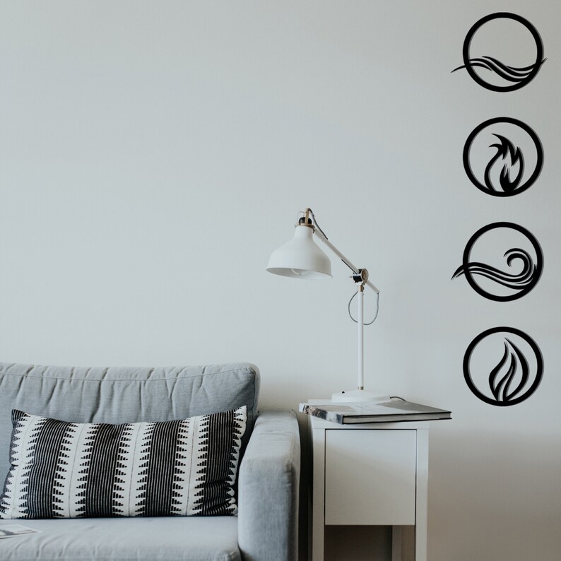 May include: Four black metal wall art pieces depicting the elements: water, fire, air, and earth. Each element is represented within a circular frame. The art is mounted on a white wall above a gray sofa and a white side table with a lamp.