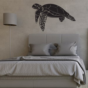 May include: A black sea turtle wall art decor. The turtle is depicted in a side profile, with detailed flippers and shell. The artwork is mounted on a textured gray wall above a bed with gray bedding.