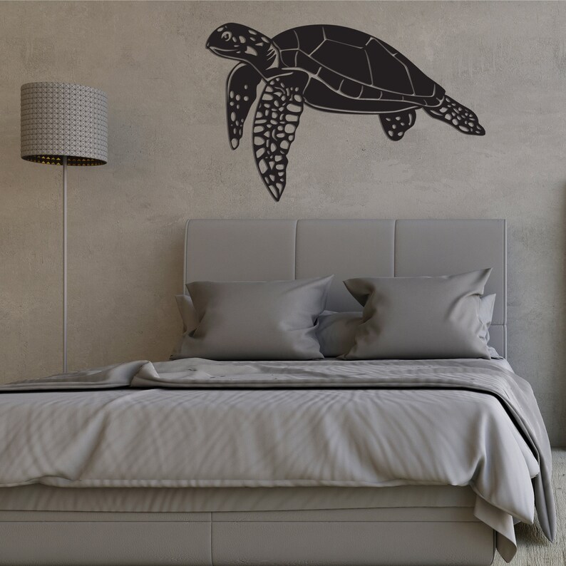 May include: A black sea turtle wall art decor. The turtle is depicted in a side profile, with detailed flippers and shell. The artwork is mounted on a textured gray wall above a bed with gray bedding.