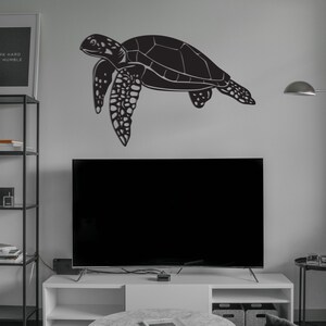 May include: A black metal sea turtle wall art decoration. The turtle is depicted in a side profile, with detailed features and a textured shell. The artwork is mounted on a light gray wall above a television.