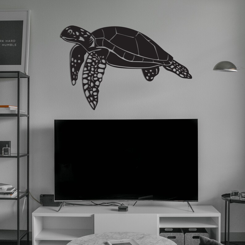 May include: A black metal sea turtle wall art decoration. The turtle is depicted in a side profile, with detailed features and a textured shell. The artwork is mounted on a light gray wall above a television.